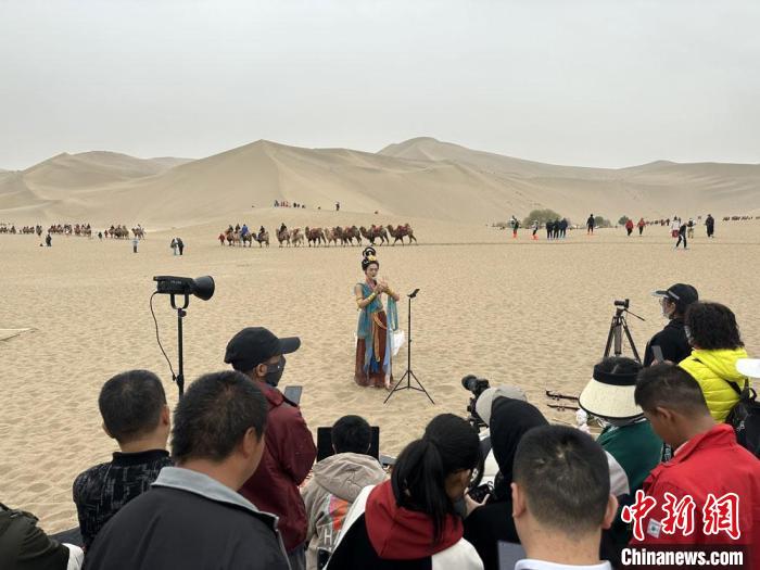 圖為2023年4月底，敦煌大漠“逐舞者”奧楠在鳴沙山月牙泉景區(qū)視頻直播，吸引游人圍觀?！●T志軍 攝