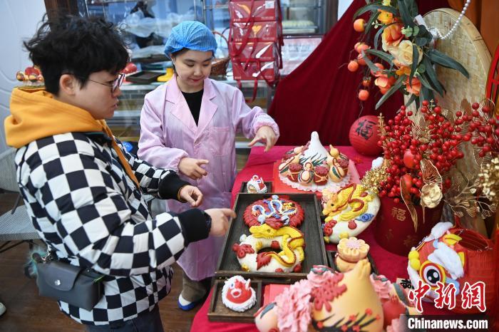 1月25日，隨著春節(jié)臨近，蘭州一花饃店“龍”元素花饃熱銷。圖為工作人員向顧客推薦“龍”元素花饃。九美旦增 攝</p><p>